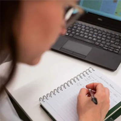 Mulher escrevendo em um caderno com uma caneta preta